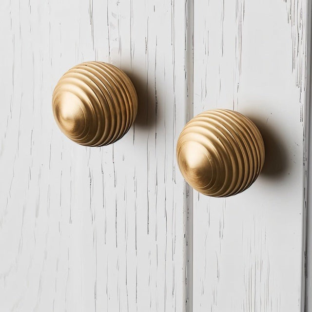 "Two gold brass ribbed knobs on a white distressed cabinet."
