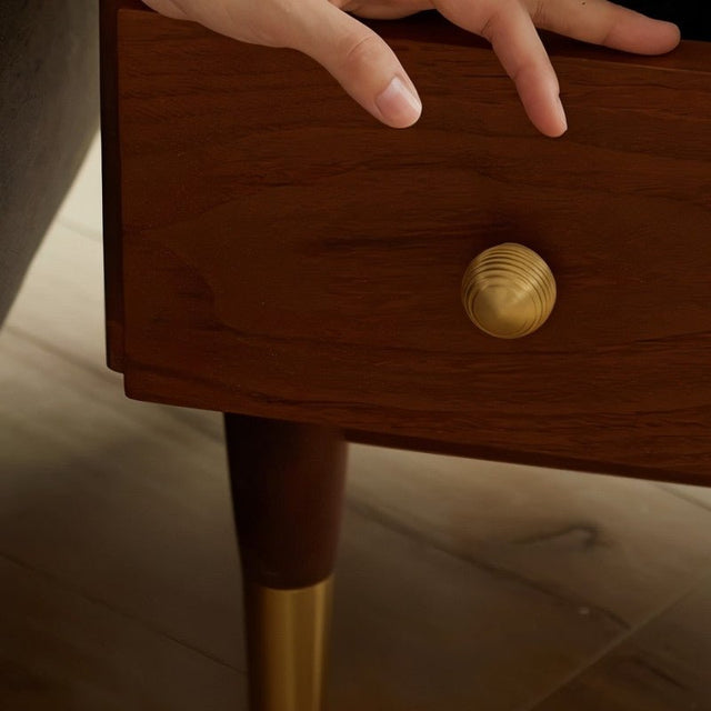 "Hand opening a brown wooden drawer with a gold brass ribbed knob."