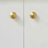 "Two gold brass ribbed knobs on a white cabinet door."