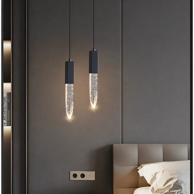 "Pair of modern pendant lights with elongated crystal diffusers and minimalist metal frames in a bedroom setting."