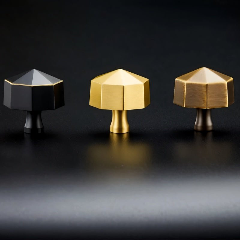 "Front view of three hexagonal brass knobs in black, gold, and bronze on a dark surface."