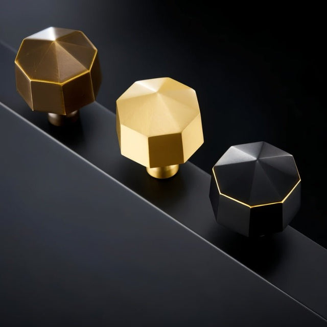 "Three hexagonal brass knobs in gold, bronze, and black on a dark surface."