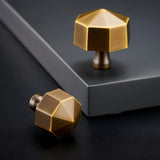 "Two gold brass hexagonal knobs on a dark surface, one upright and one tilted."