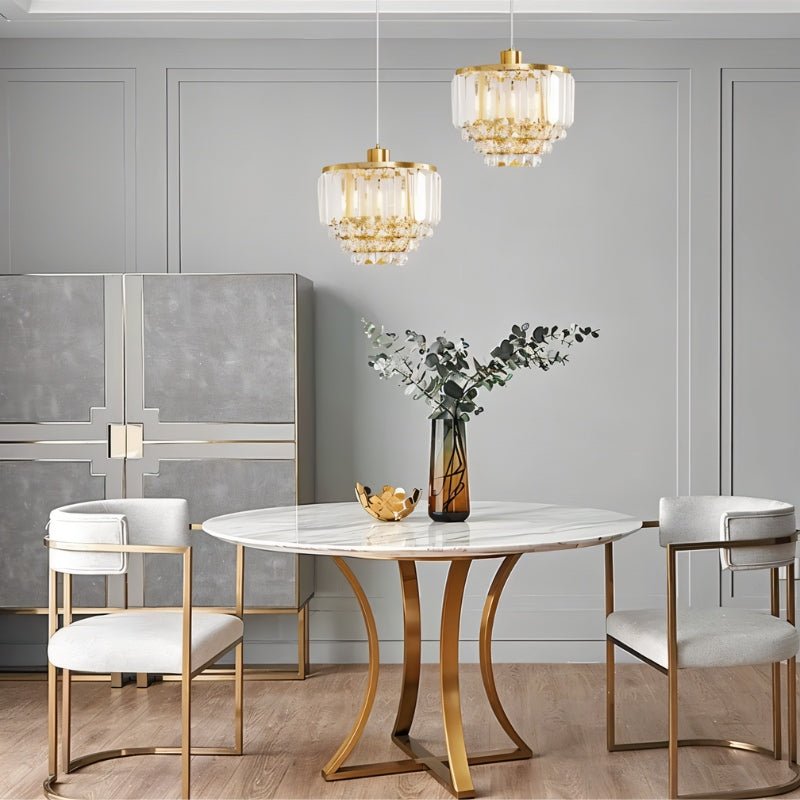 "Two tiered crystal pendant lights with brass frames, hanging in a luxurious dining room."