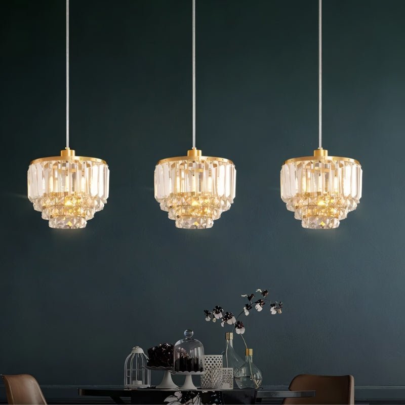 "Three tiered crystal pendant lights with brass frames, hanging against a dark background."