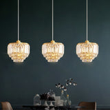 "Three tiered crystal pendant lights with brass frames, hanging against a dark background."