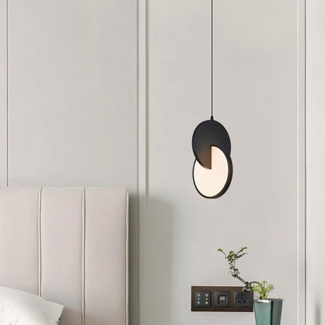 "A modern black pendant light with overlapping discs in a bedroom with a plant."