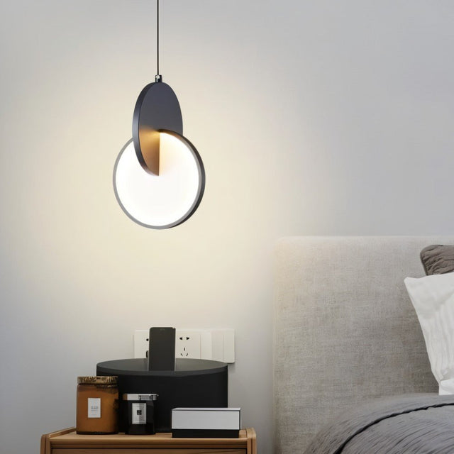 "A modern dark pendant light with overlapping discs in a bedroom above a nightstand."