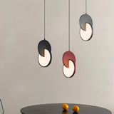 "A set of modern pendant lights with overlapping discs in various colors above a table."