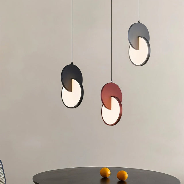 "A set of modern pendant lights with overlapping discs in various colors above a table."