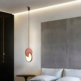 "An orange modern pendant light with overlapping discs in a bedroom with a bed and side table."
