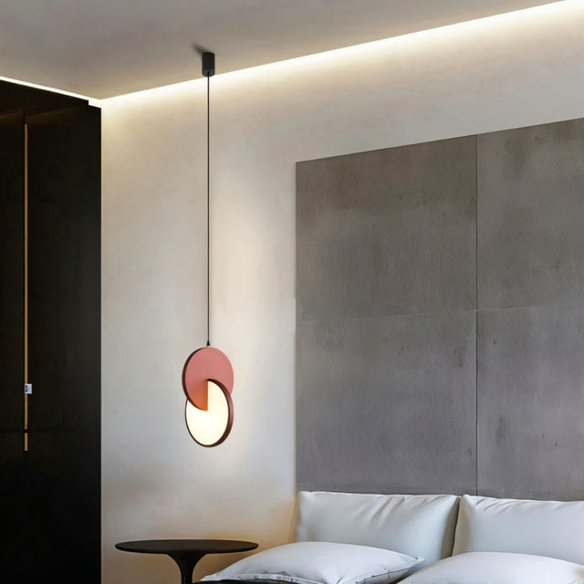 "An orange modern pendant light with overlapping discs in a bedroom with a bed and side table."