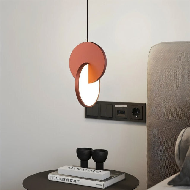 "An orange modern pendant light with overlapping discs hanging in a bedroom."