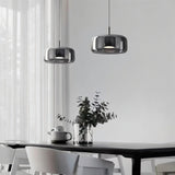 "Two modern pendant lights with smoked glass shades hanging over a dining table."