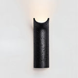"Modern Ilana wall lamp in black travertine, showcasing its unique curved design and providing a focused, elegant light."