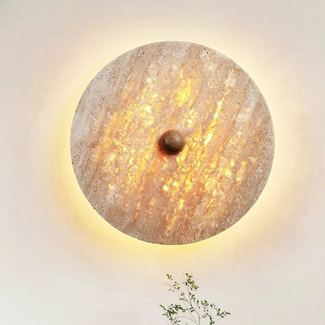 "Close-up of the Illura Wall Lamp made from travertine stone, emitting a soft, diffused backlight that creates a warm, glowing effect."