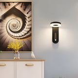 "A black wall lamp with an LED panel and a spotlight, installed in a hallway with a picture frame and a cabinet."