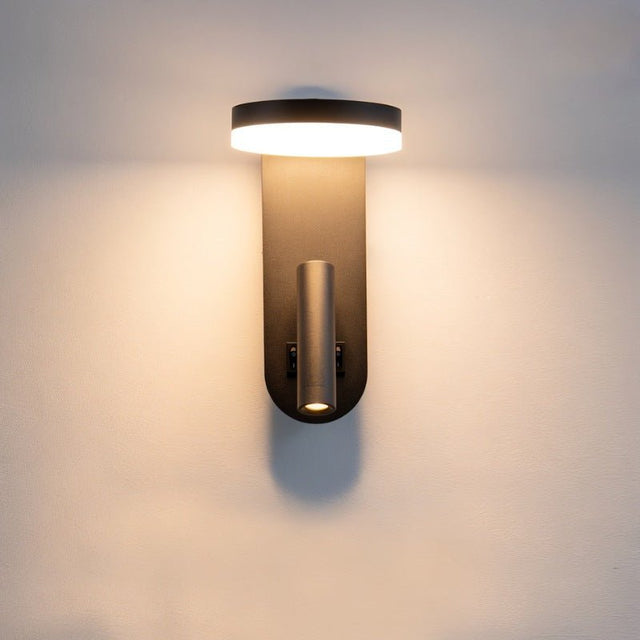 "A black wall lamp with an illuminated LED panel and a spotlight, mounted on a white wall."