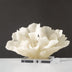 Cream-colored sculptural figurine with organic, wave-like forms on a clear acrylic base against a gray background.