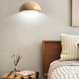 "A modern, semi-circular wall lamp made of yellow travertine, mounted on a wall beside a bed, casting a soft, ambient light on the side of the room."