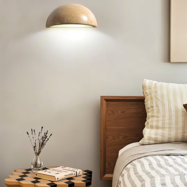"A modern, semi-circular wall lamp made of yellow travertine, mounted on a wall beside a bed, casting a soft, ambient light on the side of the room."