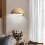"A modern, semi-circular wall lamp made of yellow travertine, mounted on a wall near a window in a living room, providing a soft, ambient light."
