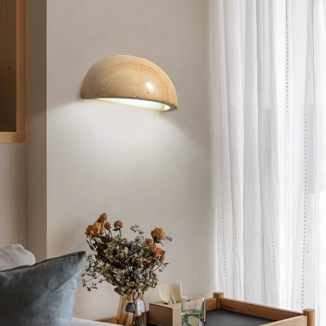 "A modern, semi-circular wall lamp made of yellow travertine, mounted on a wall near a window in a living room, providing a soft, ambient light."