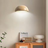 "A modern, semi-circular wall lamp made of yellow travertine, mounted on a wall above a cabinet in a living room, providing a warm, ambient glow."
