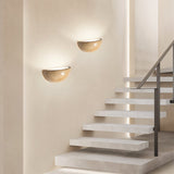 "Two modern, semi-circular wall lamps made of yellow travertine, mounted on a wall beside a stairway, providing soft, ambient lighting." 