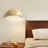 "A modern, semi-circular wall lamp made of yellow travertine, emitting a warm glow in a minimalist bedroom setting."
