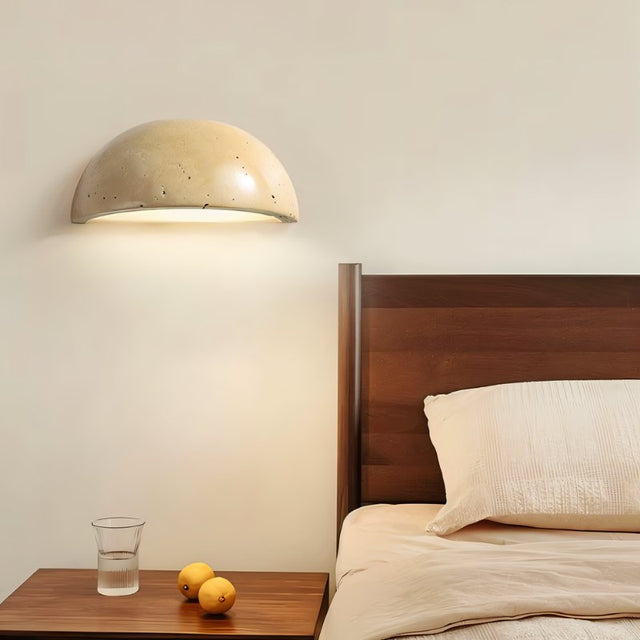 "A modern, semi-circular wall lamp made of yellow travertine, emitting a warm glow in a minimalist bedroom setting."
