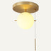 Brass ceiling light fixture with cream-colored spherical glass shade on beige background.