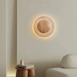 "Sculptural wall lamp with a travertine stone ring and wood center in a modern living room setting."