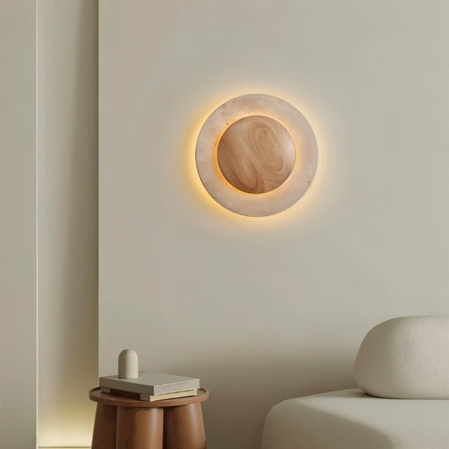 "Sculptural wall lamp with a travertine stone ring and wood center in a modern living room setting."