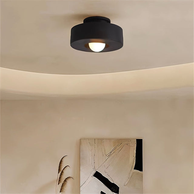 "Black circular flush mount ceiling light in a room with artwork."
