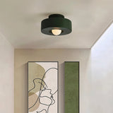 "Green circular flush mount ceiling light in a hallway with artwork."