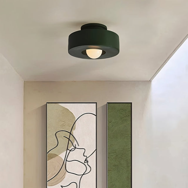 "Green circular flush mount ceiling light in a hallway with artwork."