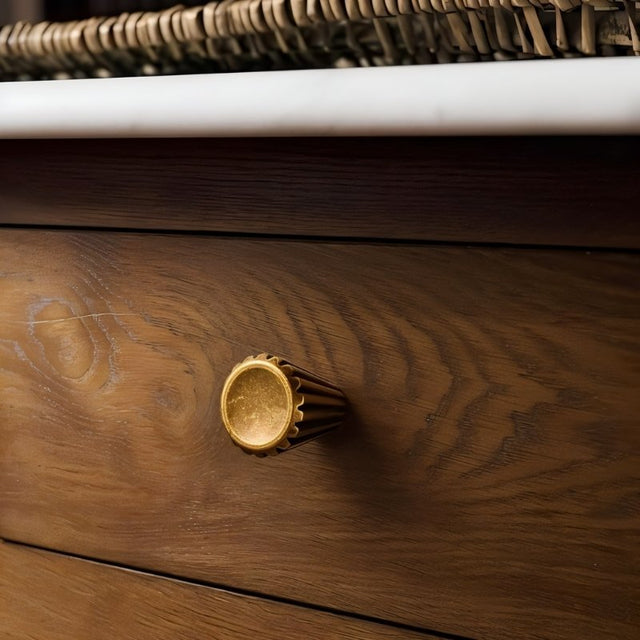 "A contemporary brass cone-shaped knob with sleek vertical grooves, installed on a wooden dresser, showcasing its smooth, polished circular face."