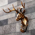 Golden bronze deer head figurine with ornate antlers mounted on a gray striped wall background.