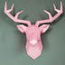Pink low-poly deer head figurine with geometric faceted design mounted on sage green wall.