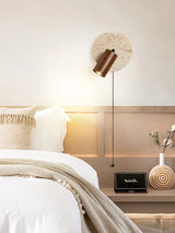 "Yellow travertine round wall lamp with wooden cylindrical shade and pull chain above a bed, modern bedside reading light."