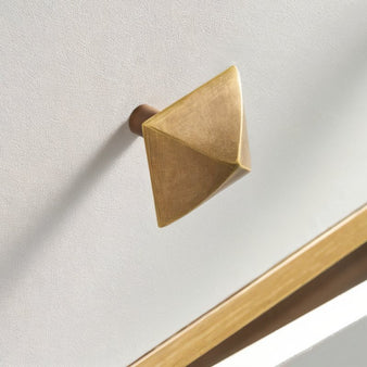 "Pyramid-shaped brass knob on a white cabinet."