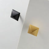 "Pyramid-shaped brass knobs in black and gold finishes on a white surface."