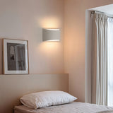 "Modern curved rectangular gypsum wall lamp providing soft ambient light in a contemporary bedroom with a window and sheer curtains."