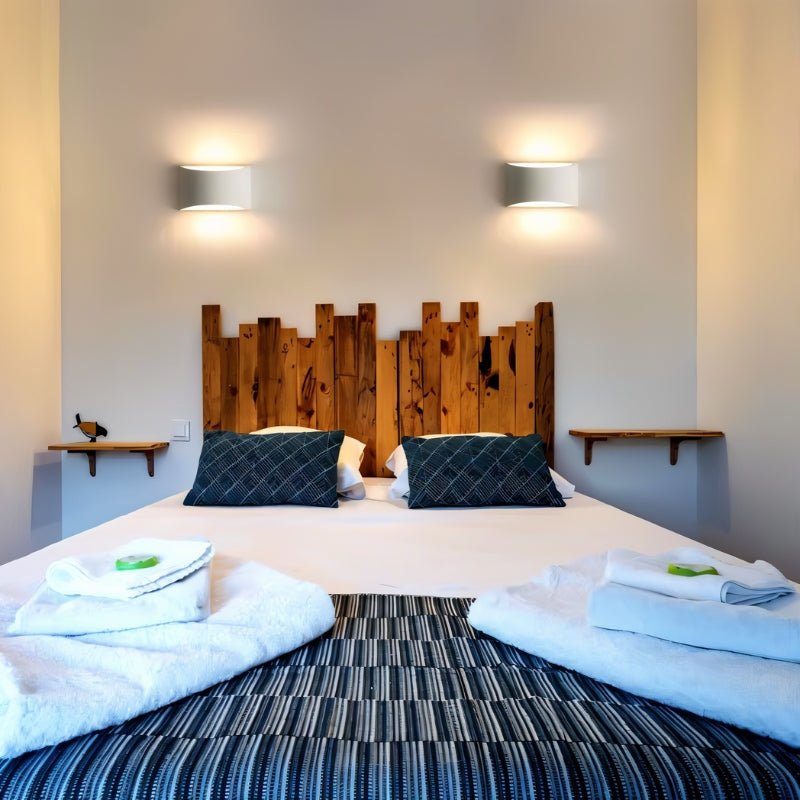 "Pair of modern curved rectangular gypsum wall lamps flanking a rustic wooden headboard in a contemporary bedroom, casting soft ambient light."