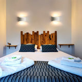 "Pair of modern curved rectangular gypsum wall lamps flanking a rustic wooden headboard in a contemporary bedroom, casting soft ambient light."