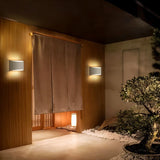 "Pair of modern curved rectangular gypsum wall lamps providing soft ambient lighting in a Japanese-inspired indoor garden setting."