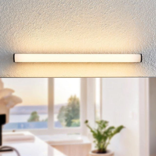 "Illuminated modern wall lamp with a white diffuser, mounted on a textured wall above a blurred bathroom view."