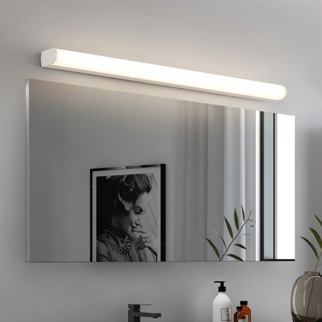 "White modern wall lamp illuminating a bathroom mirror with a picture frame and toiletries reflected."