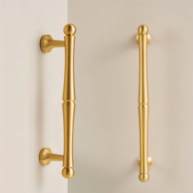 "Two brass pull bar handles mounted on a white surface."